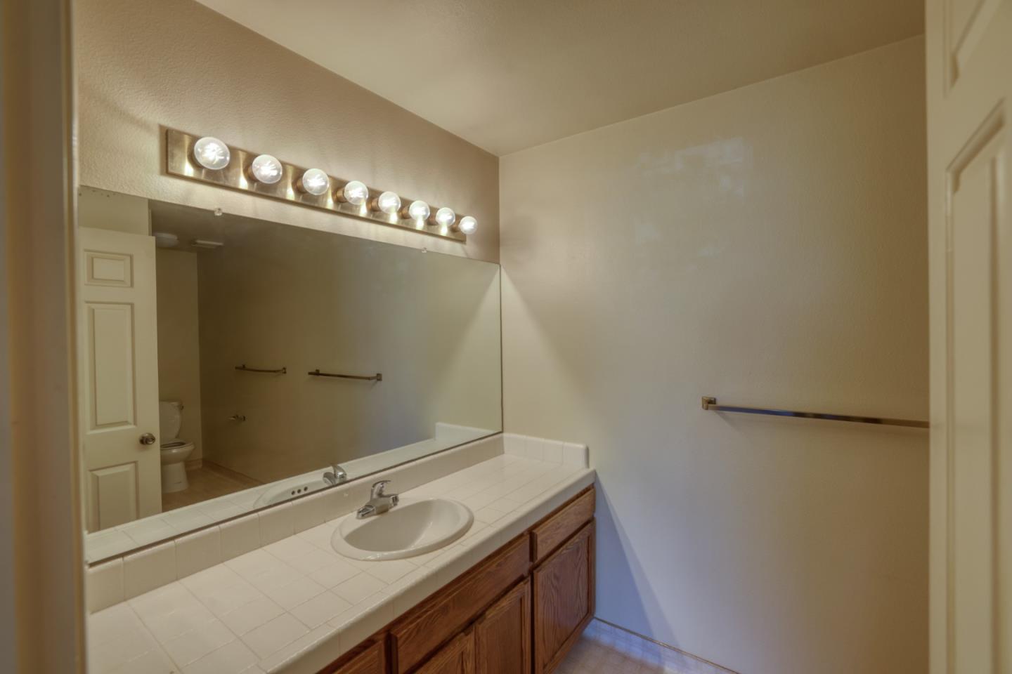 Bathroom vanity with a long tiled counter, oval sink, wood cabinets, and large illuminated mirror.