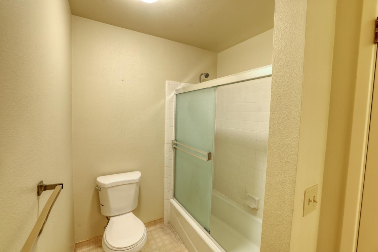 Bathroom with a toilet beside a bathtub and frosted sliding glass shower door.