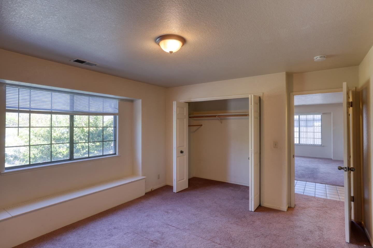 Empty carpeted bedroom with a wide window, built-in bench, and open closet.