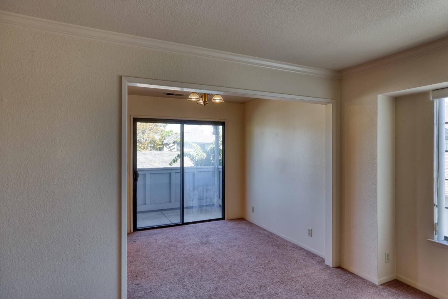 Empty carpeted living room with a sliding glass door opening to a patio or balcony.