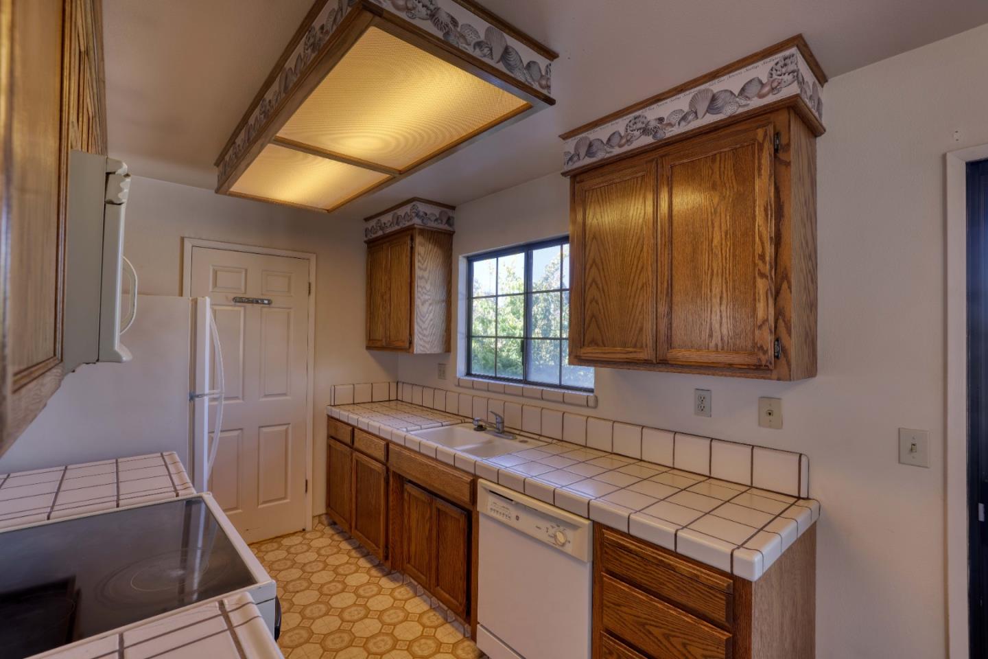 Kitchen with oak cabinets, tiled counters, white appliances, and a decorative wood-trimmed ceiling hood.