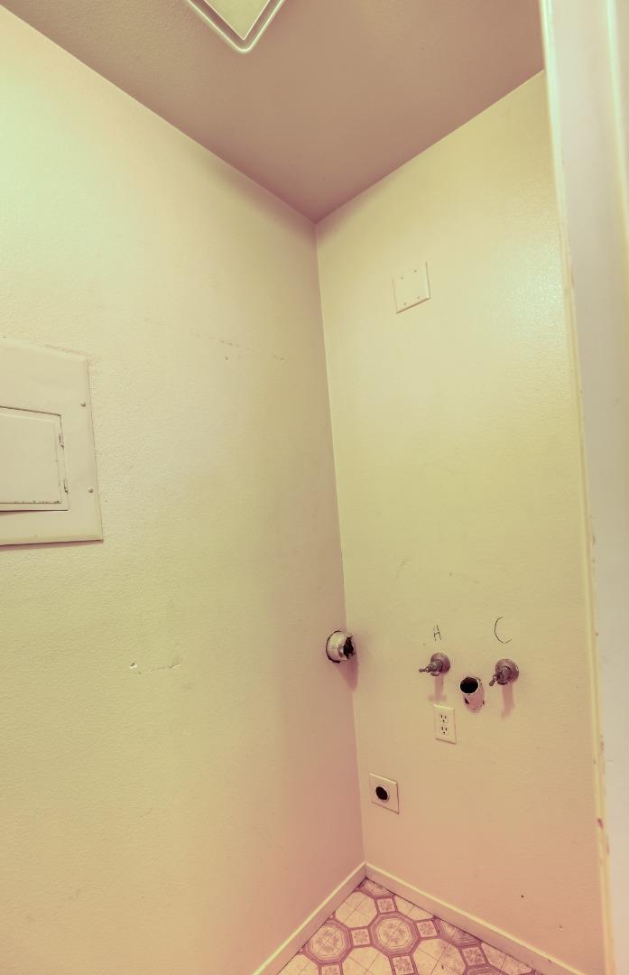 Empty laundry area with exposed washer hookups and patterned tile flooring.
