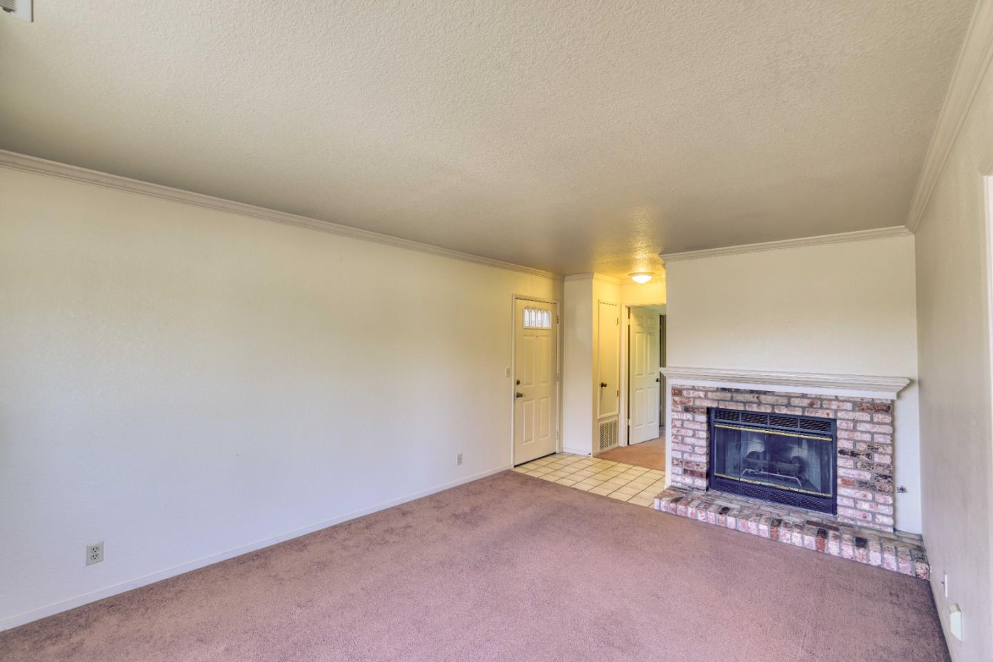 Empty living room with a brick fireplace, carpeted floor, and tiled entry.