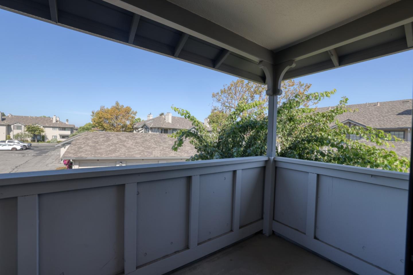 Covered balcony overlooking nearby homes and trees beneath a clear blue sky.