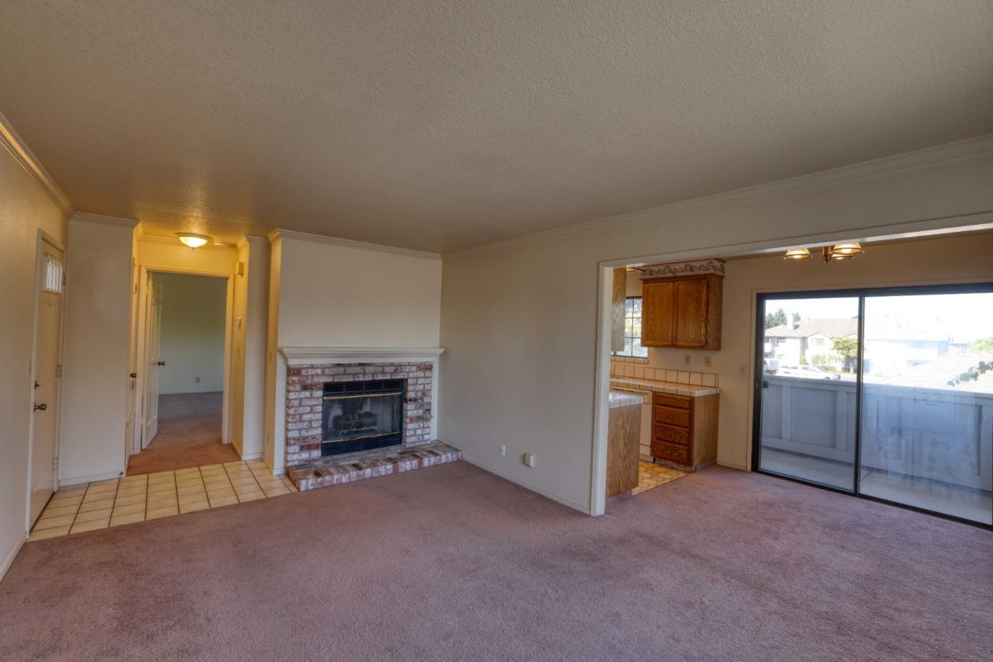 Unfurnished living room with a brick fireplace, adjoining kitchen, and sliding glass door to a balcony.