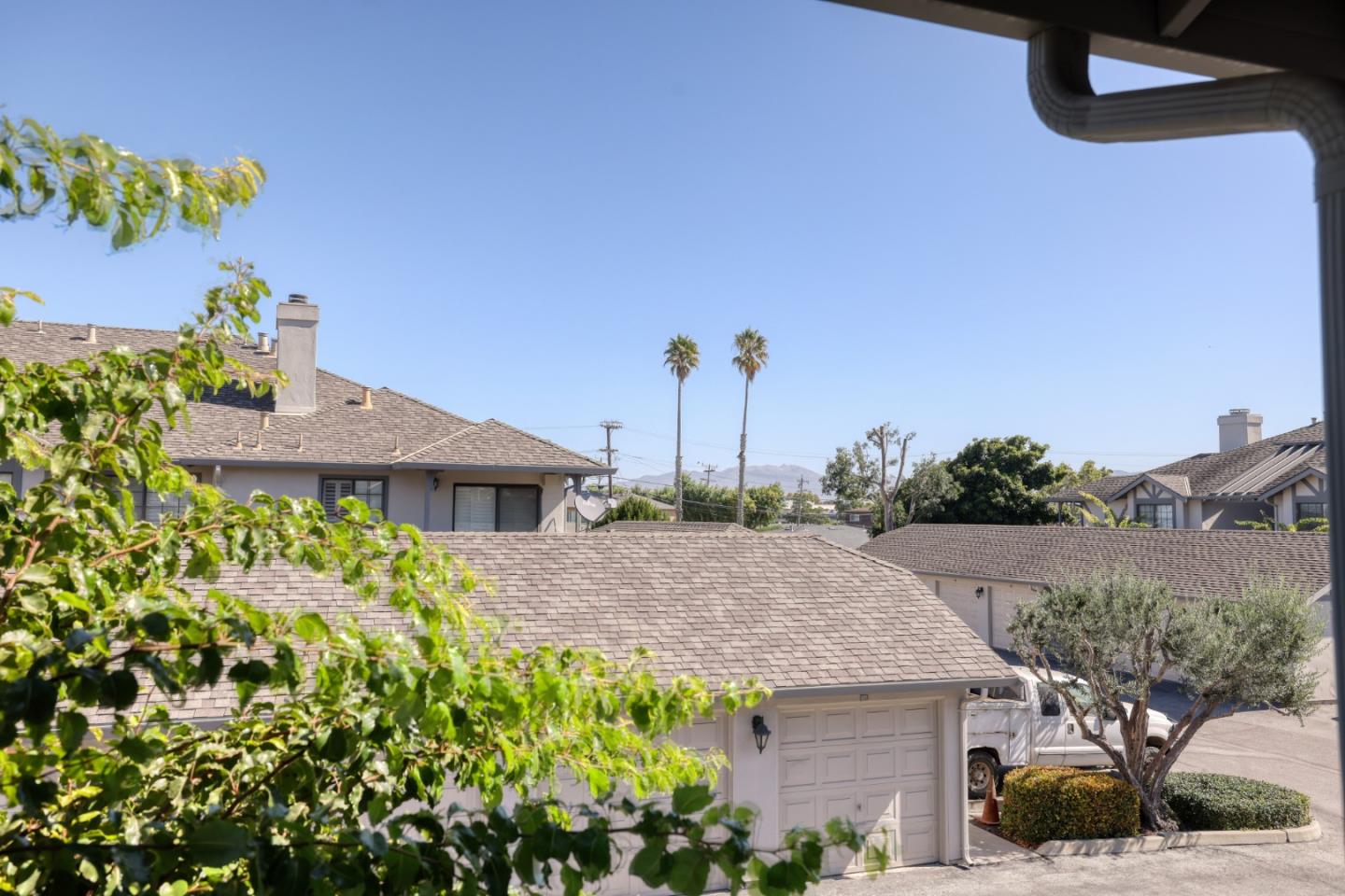 View over neighboring rooftops and a garage toward palm trees and distant hills.