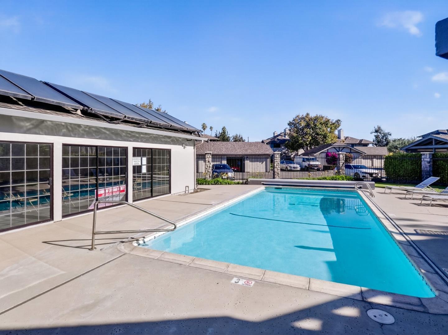 Outdoor swimming pool with a broad concrete deck and solar panels on the adjacent building.