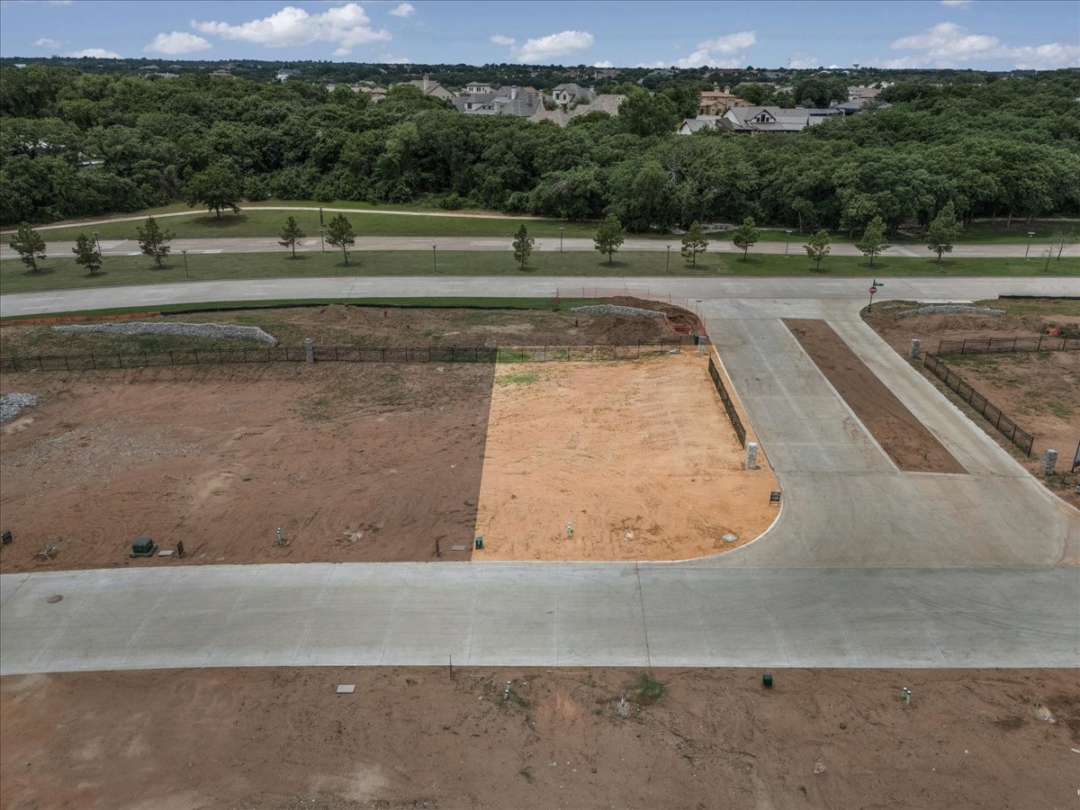 Vacant graded lots beside newly paved streets, with trees and homes in the distance.