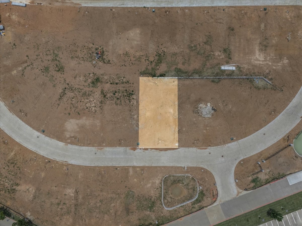 Vacant dirt lot bordered by curved paved streets, with a pale rectangular section in the center.
