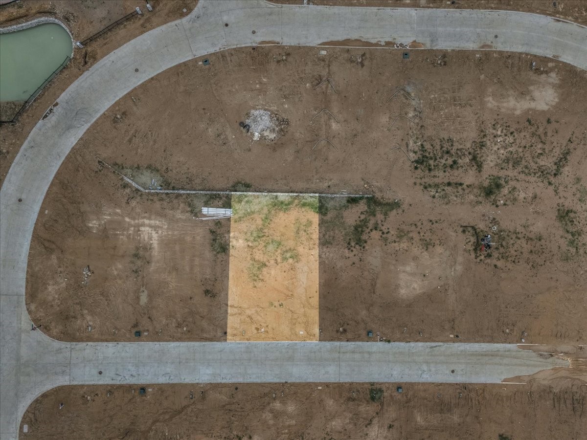 Highlighted bare lot bordered by paved subdivision roads, with a small pond nearby.