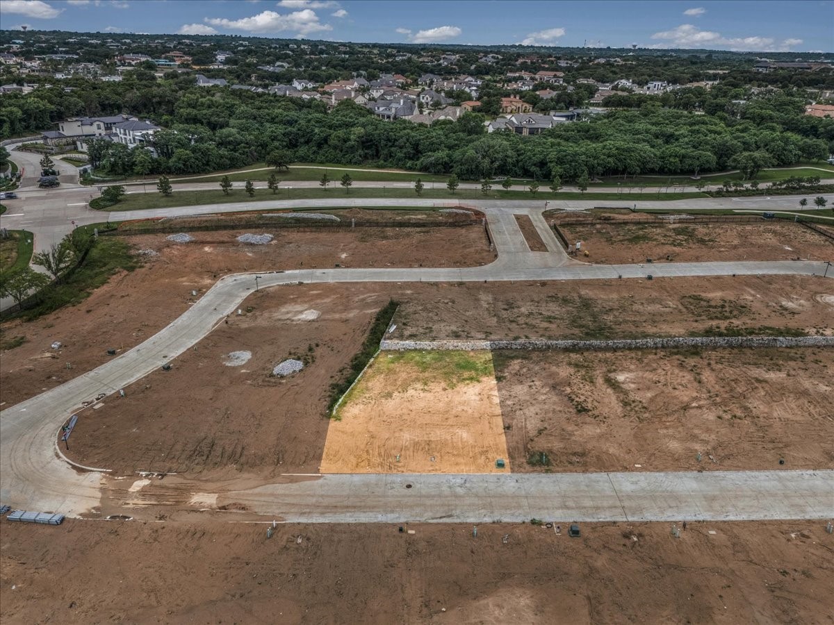 Aerial view of graded residential lots and new streets beside a wooded neighborhood.