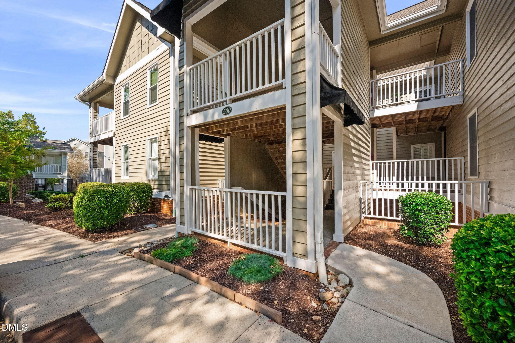 Multi-unit residential building with white-railed balconies, covered entryways, and landscaped walkways.