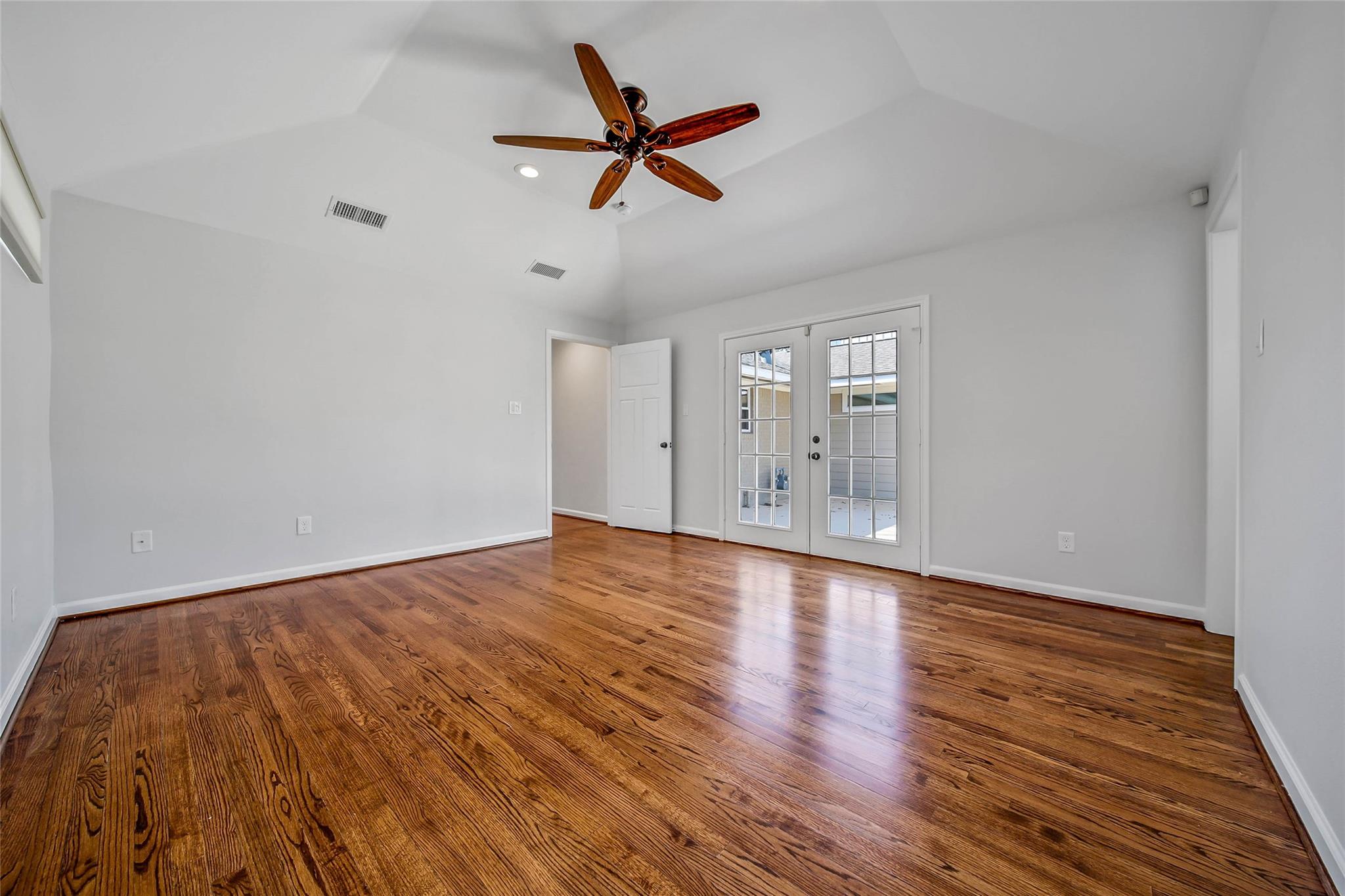 Empty room with polished hardwood floors, a vaulted ceiling, and glass-paneled French doors.