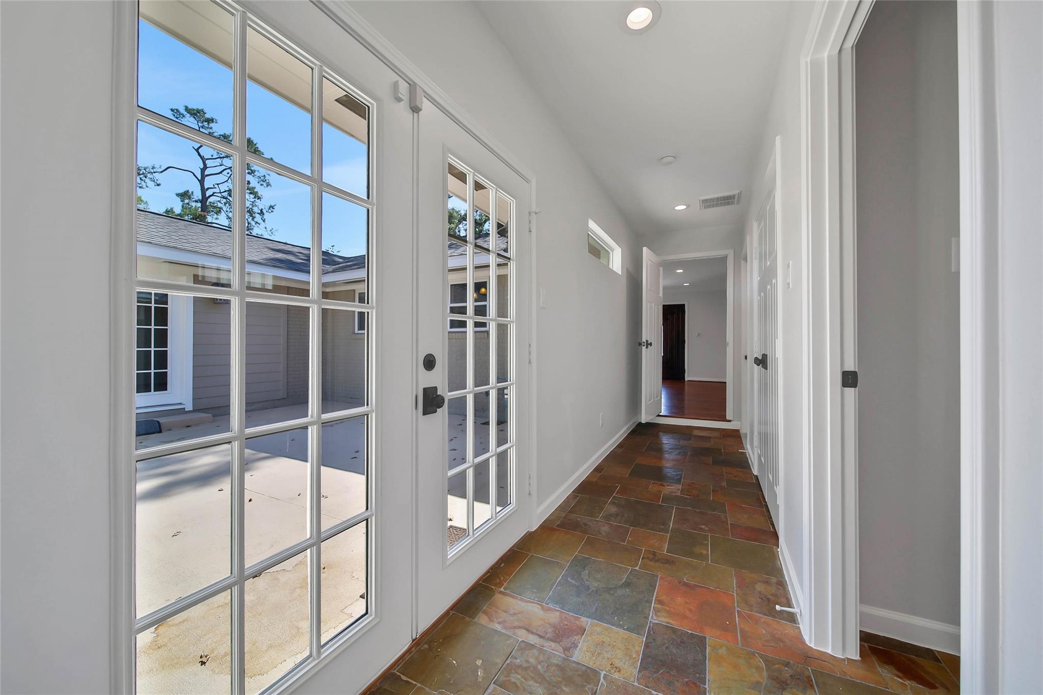 Unfurnished hallway with multicolored stone tile floors and glass-paneled doors overlooking a courtyard.