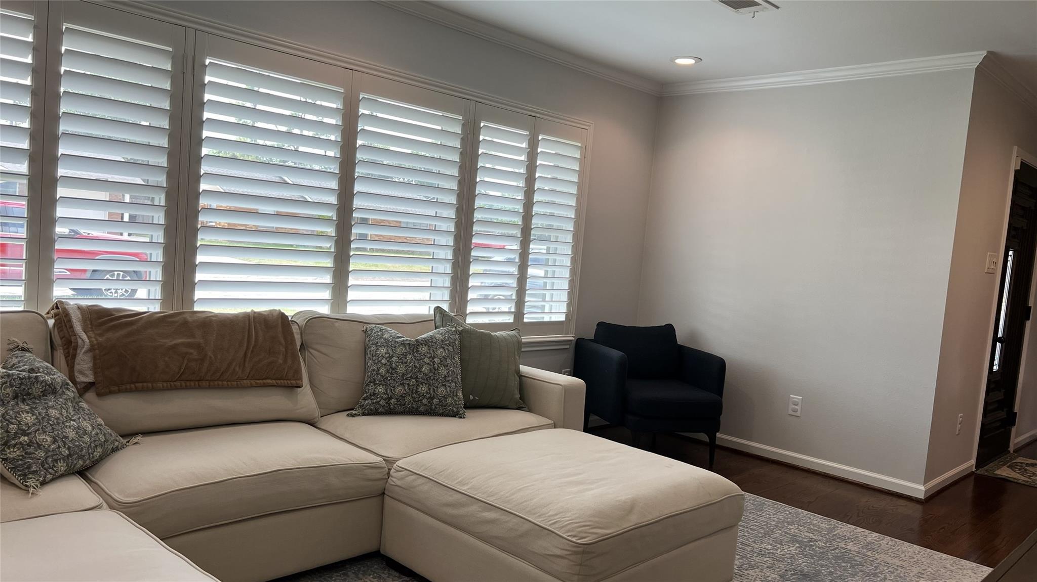 Living room with a cream sectional, dark armchair, and tall plantation-shuttered windows.