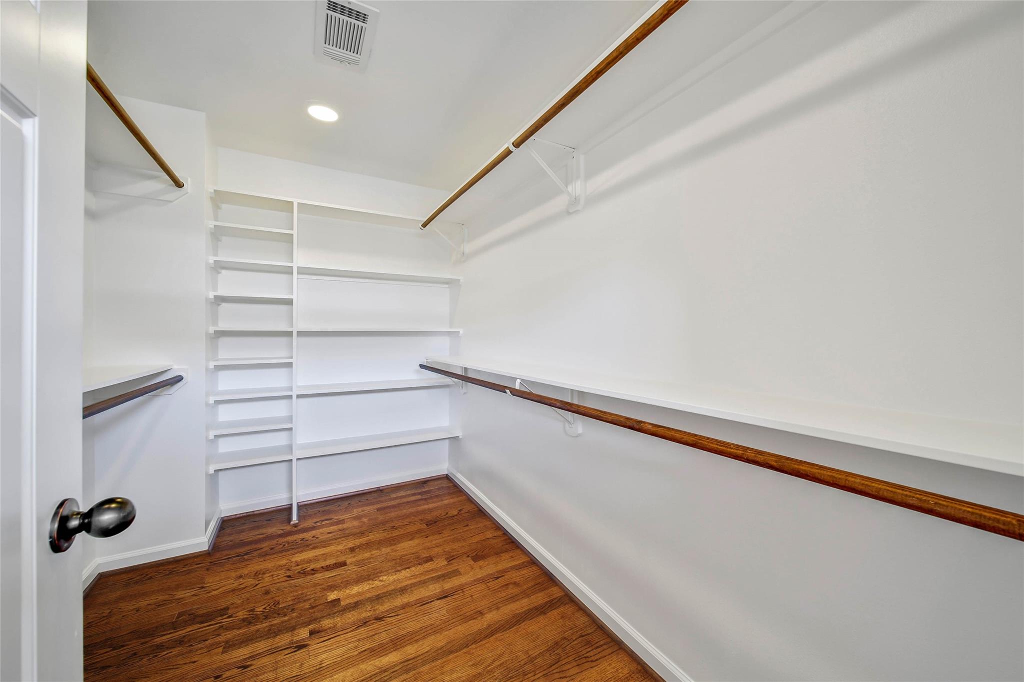 Walk-in closet with white built-in shelves, wood hanging rods, and dark hardwood flooring.