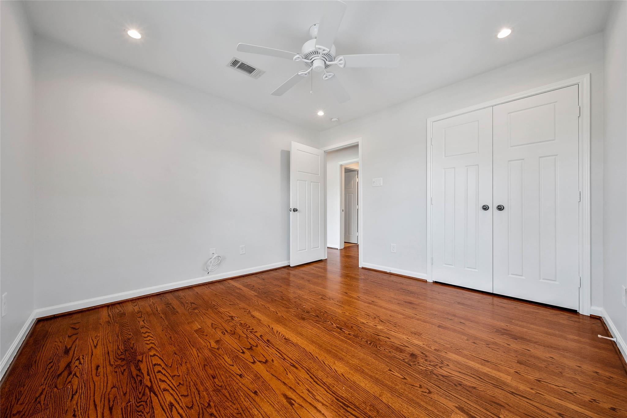 Empty bedroom with hardwood floors, a white ceiling fan, and double closet doors.