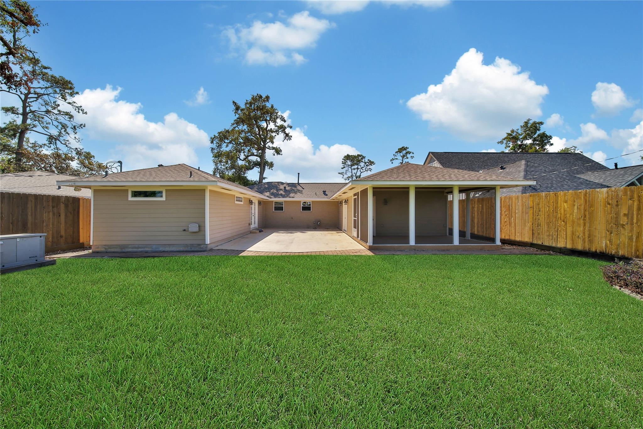 Fenced backyard with a broad lawn, concrete patio, and covered screened porch.