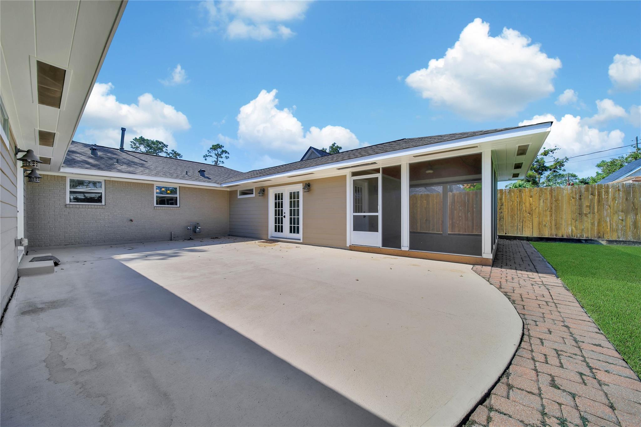 Home’s rear courtyard with a broad concrete patio, screened porch, and brick path beside the lawn.