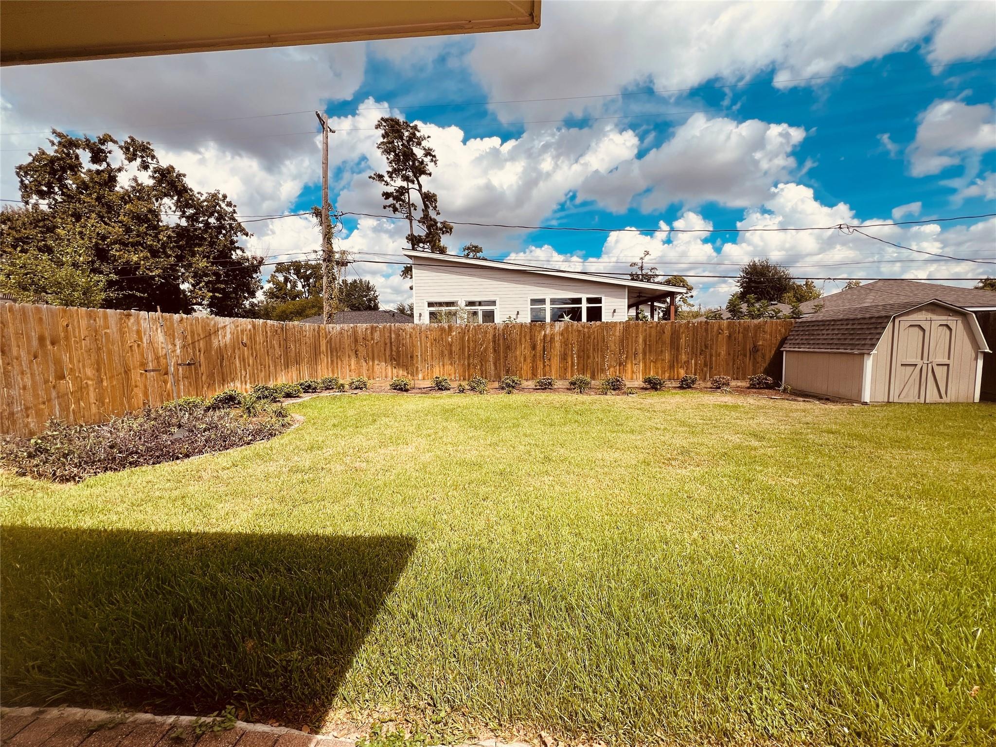 Fenced backyard with a broad lawn, garden beds, and a small storage shed.