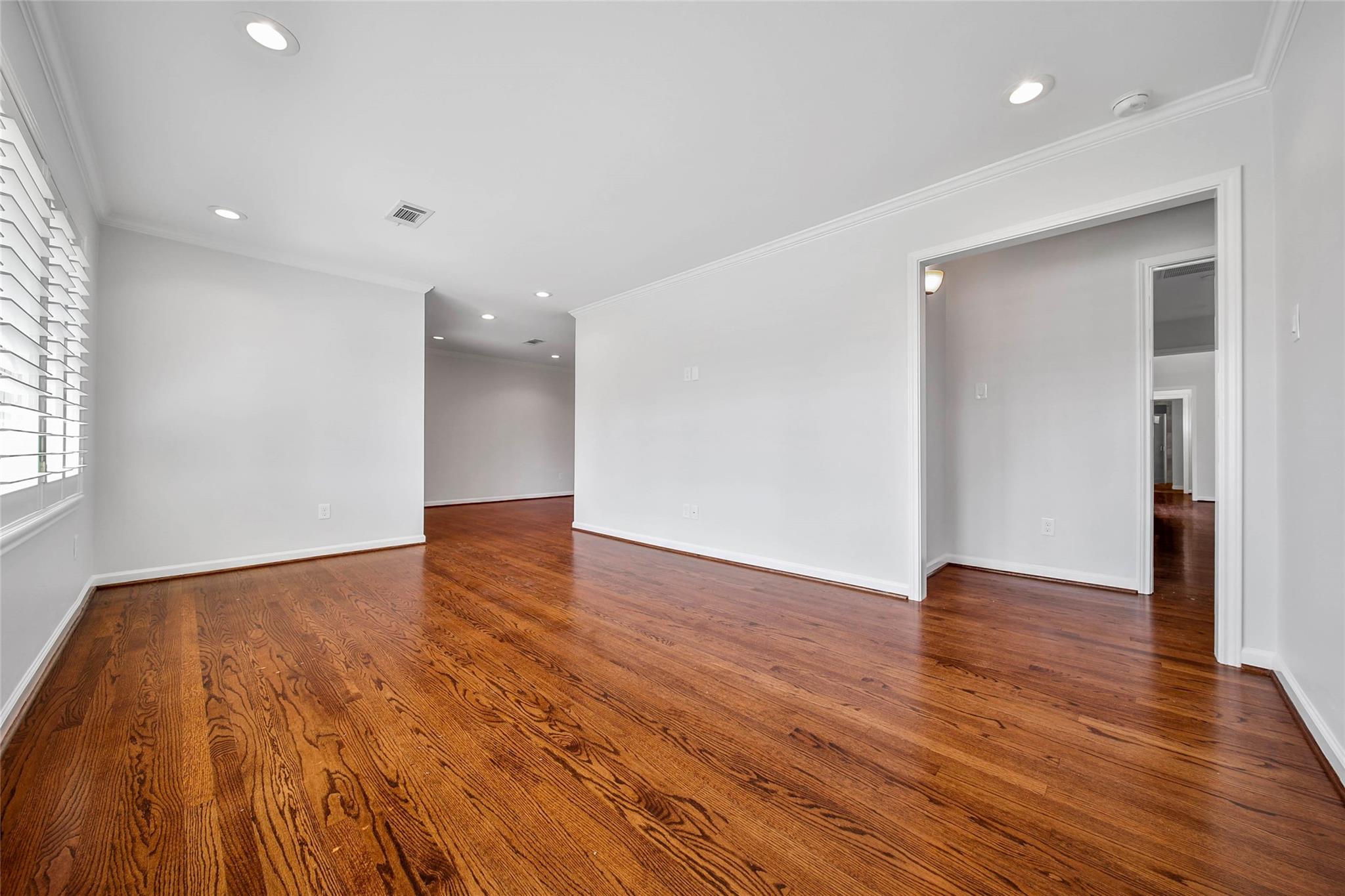 Vacant room with polished hardwood floors, white walls, and a window with shutters.