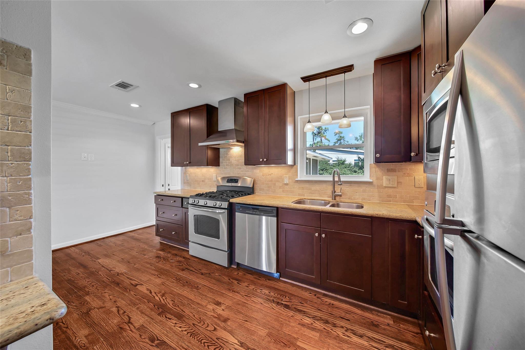 Kitchen with dark wood cabinets, stainless steel appliances, and a tan brick backsplash.