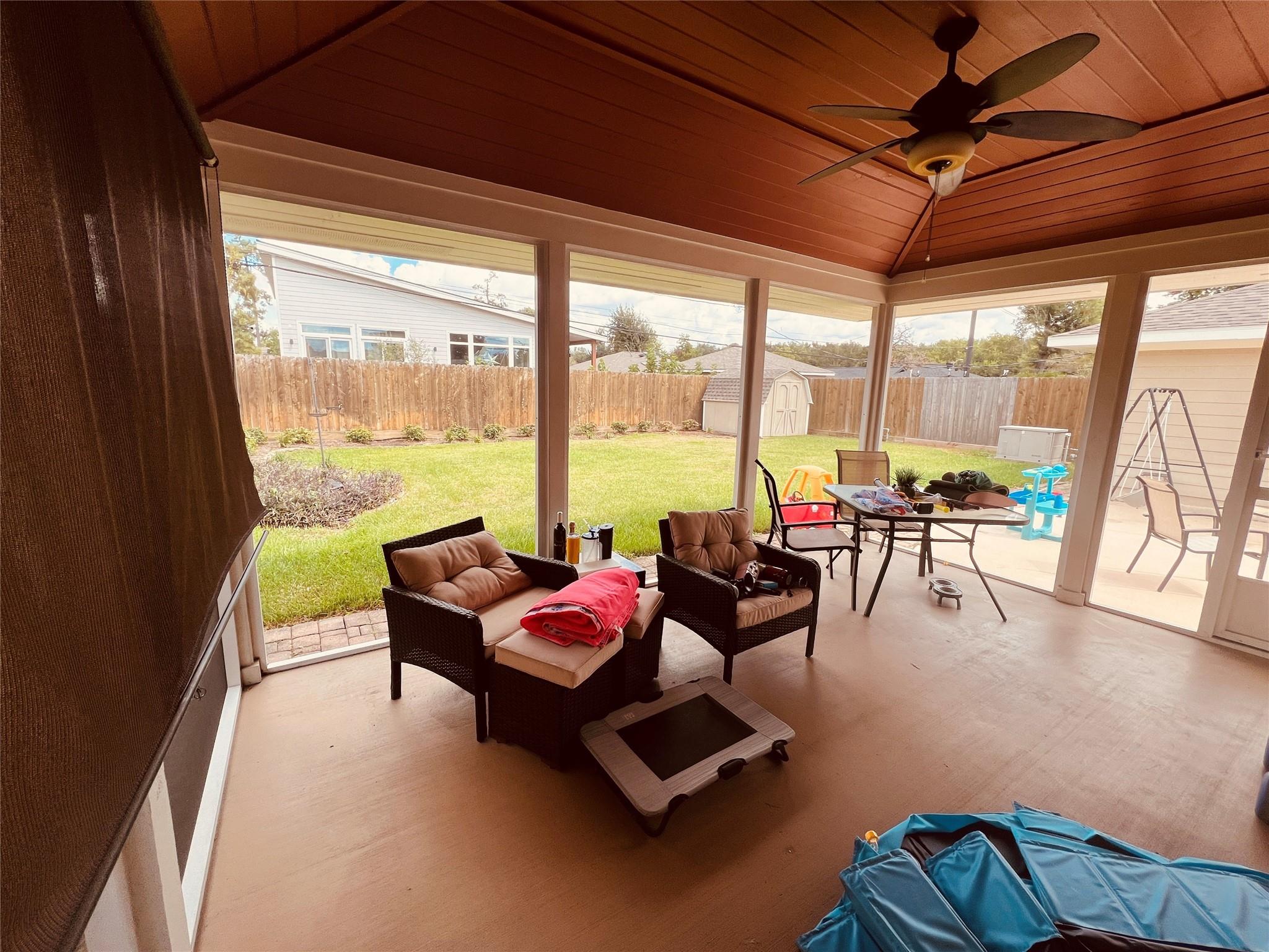 Screened-in patio with wicker seating and a ceiling fan, overlooking a fenced backyard.