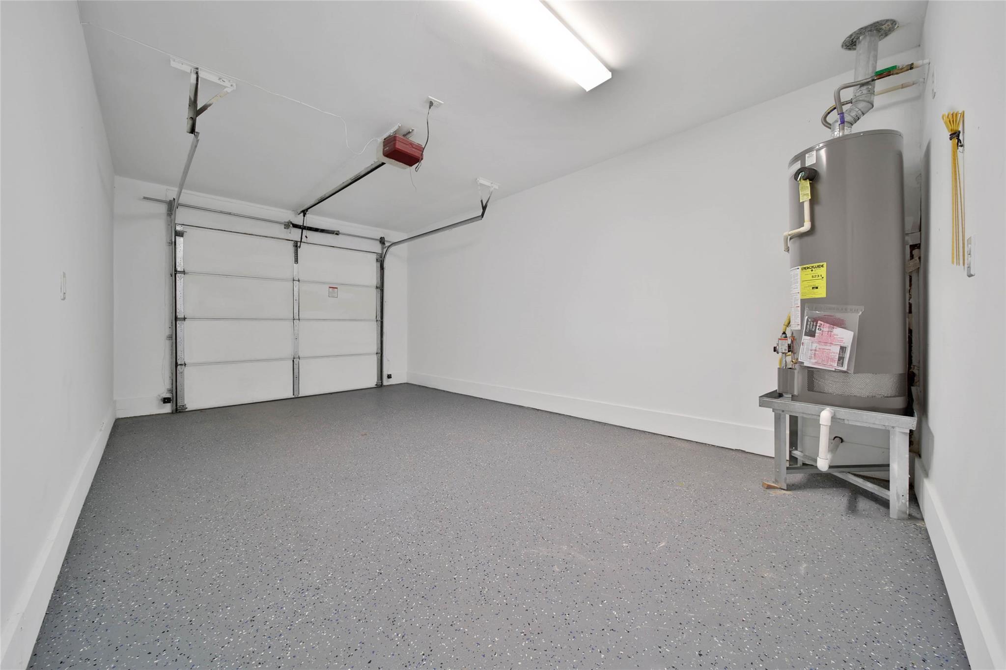 Empty garage with a speckled epoxy floor and tank water heater.