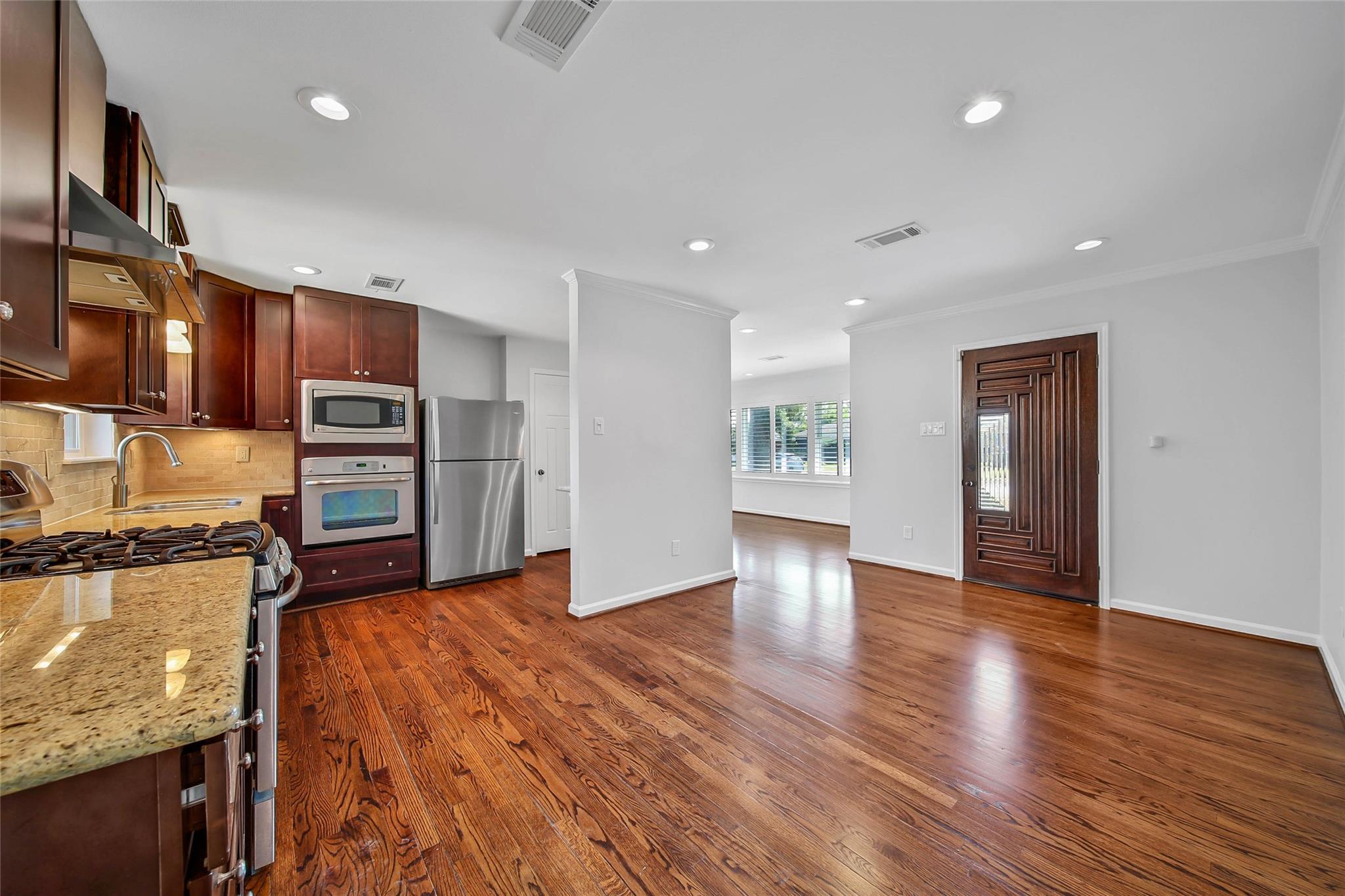 Kitchen with dark wood cabinets, granite counters, stainless appliances, and hardwood floors opening to the entryway.