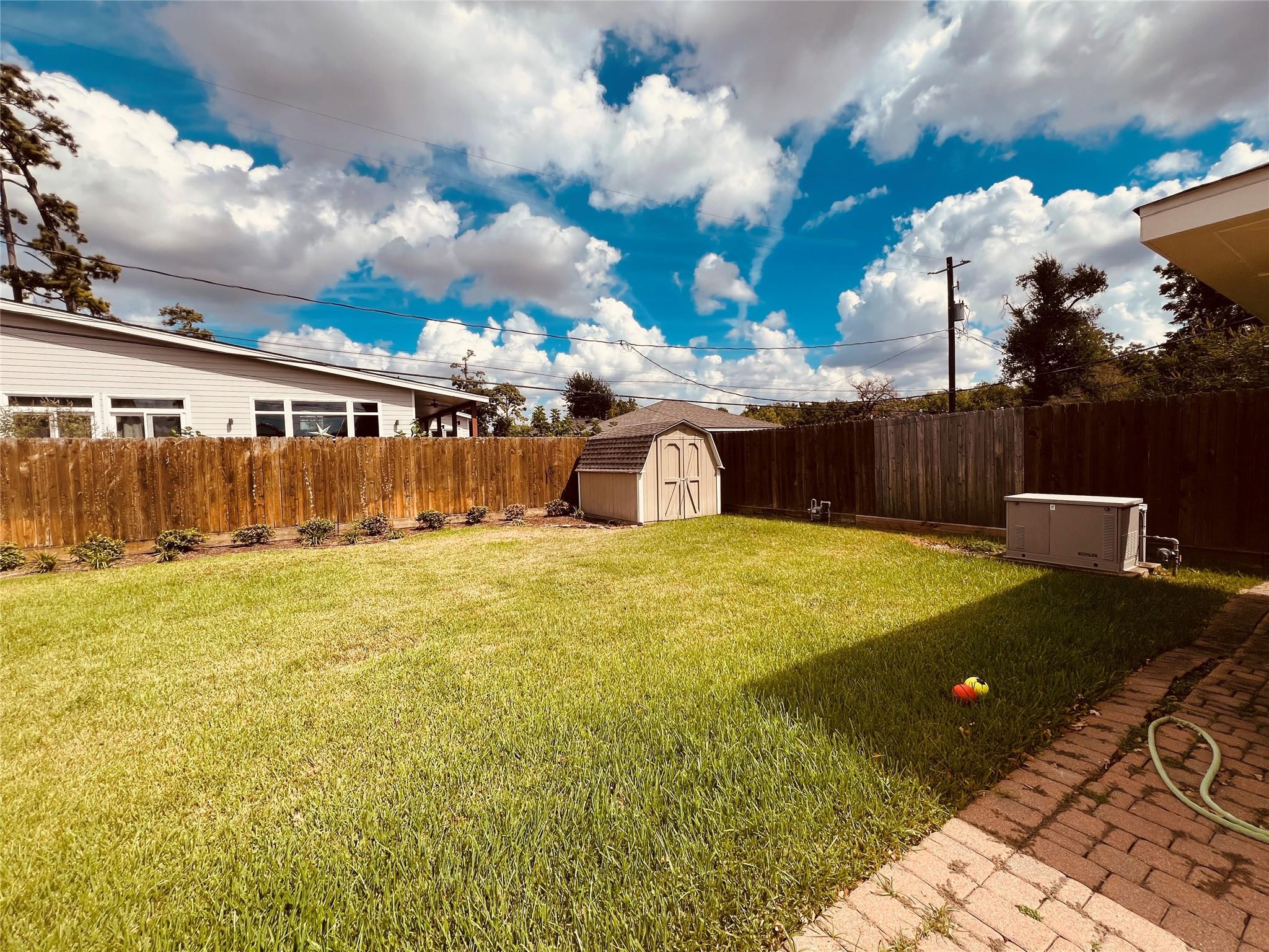 Fenced backyard with a broad lawn, small storage shed, and brick-paved patio.