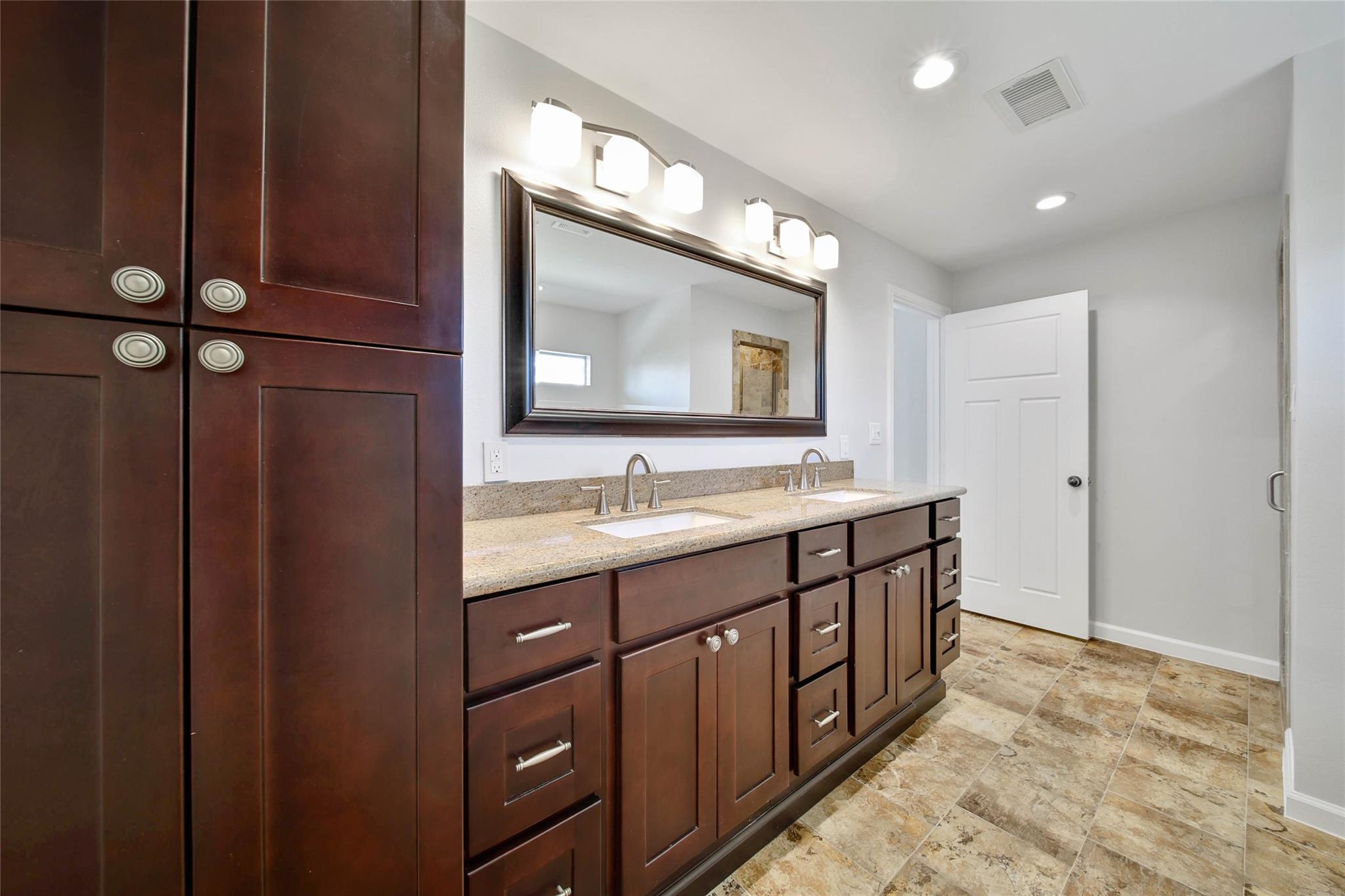 Bathroom vanity with dark wood cabinets, two sinks, granite counter, and a large framed mirror.