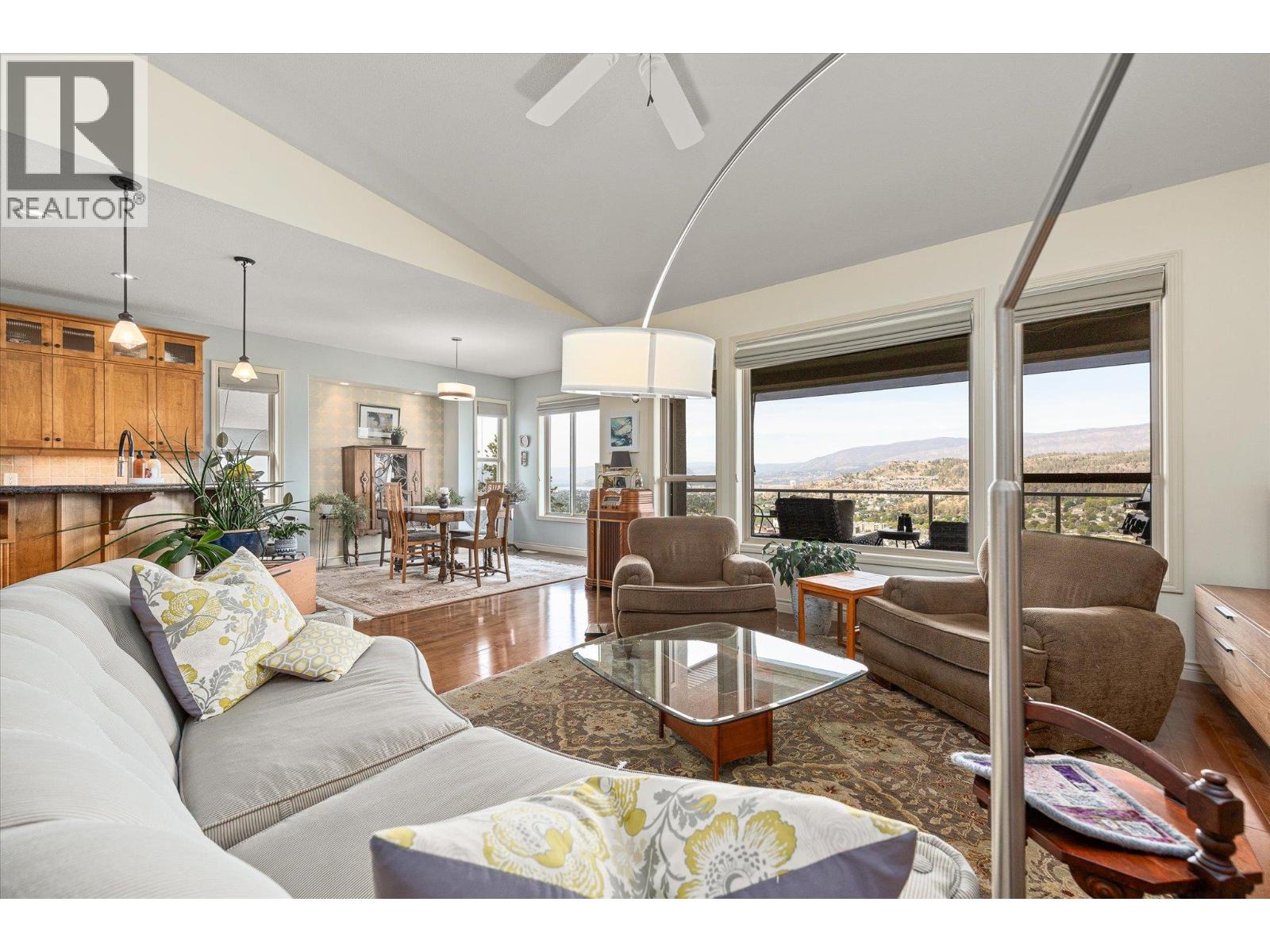 Open-plan living room with vaulted ceiling, large windows, and distant lake and hillside views.