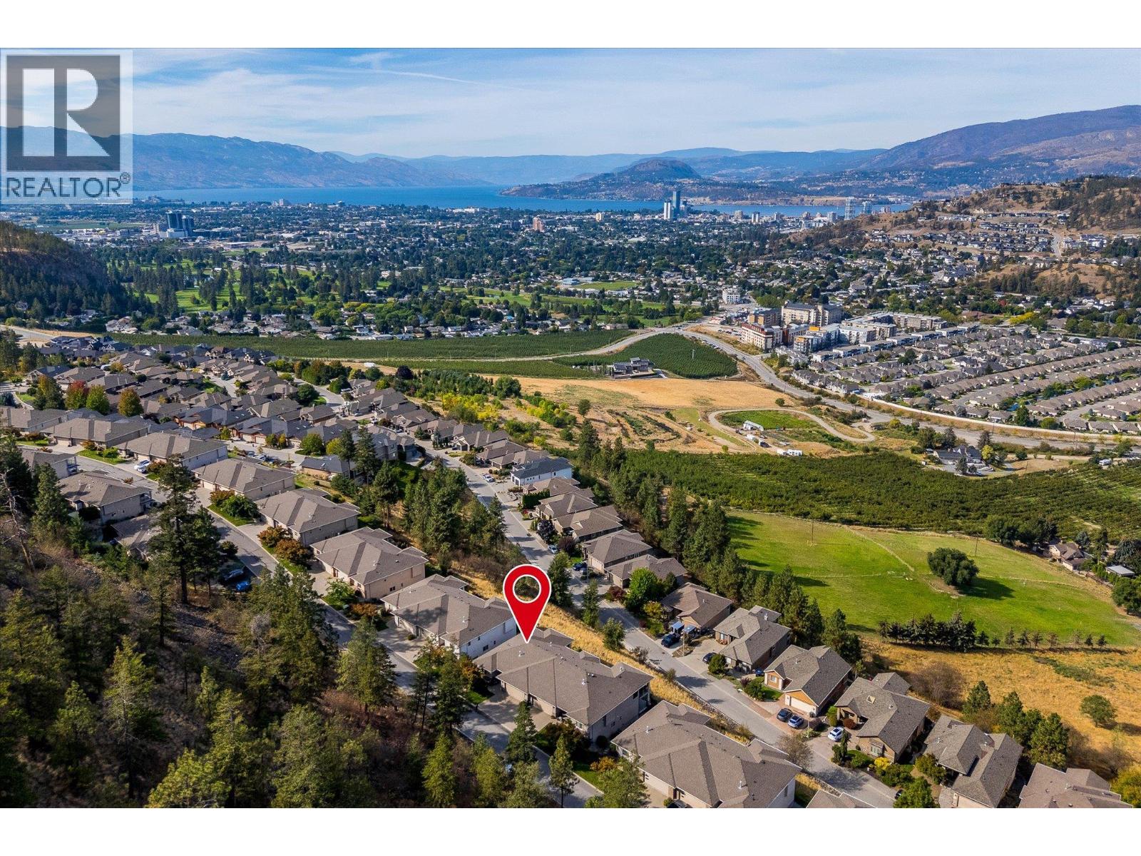 Aerial view of a Kelowna neighborhood, with a home marked by a red pin and Okanagan Lake beyond.