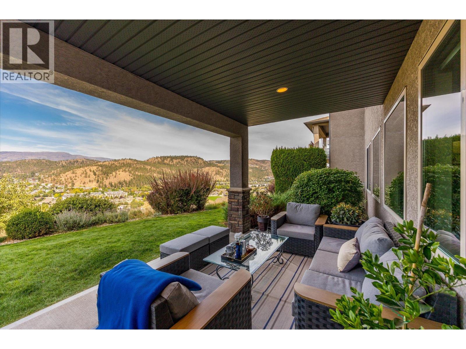 Covered patio with wicker seating overlooks a landscaped lawn, residential valley, and rolling hills.