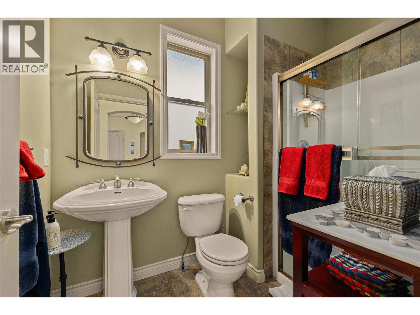 Bathroom with a pedestal sink, large mirror, and glass-enclosed tiled shower.