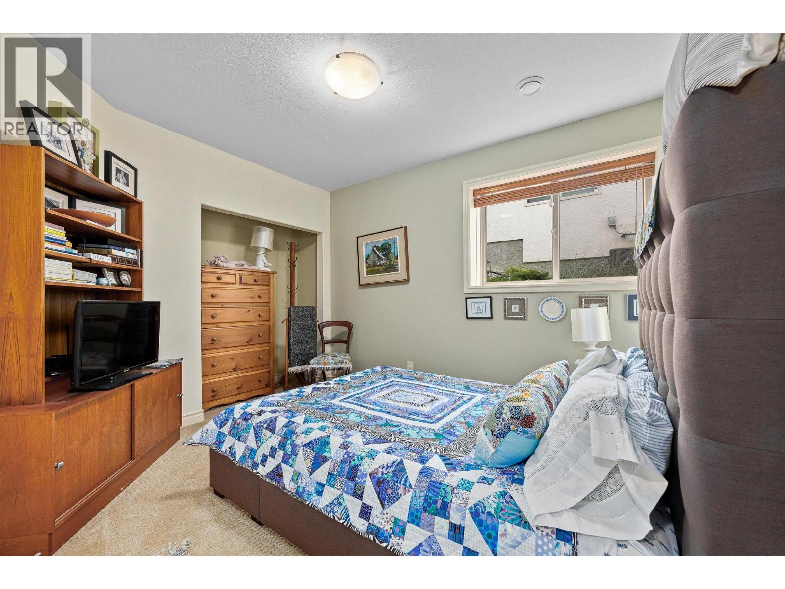 Furnished bedroom with a colorful patchwork quilt, wooden dresser, and entertainment center.