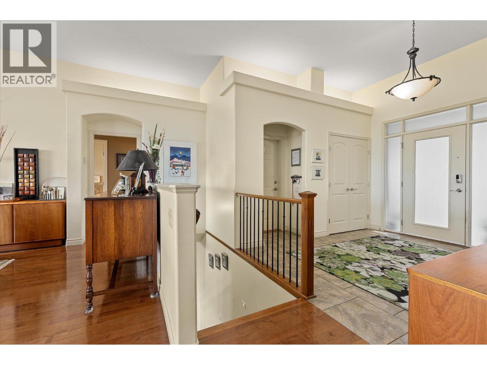 Condo entry hall with a tiled foyer, glass-paneled front door, and railing around a stairwell.