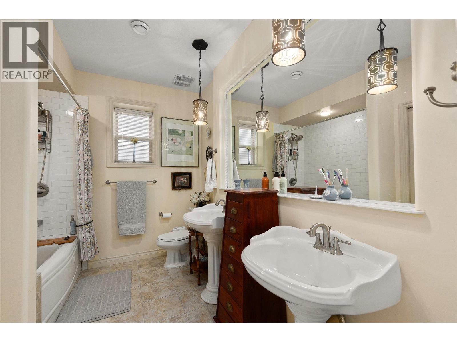 Bathroom with two pedestal sinks, a large mirror, and a bathtub with tiled shower.