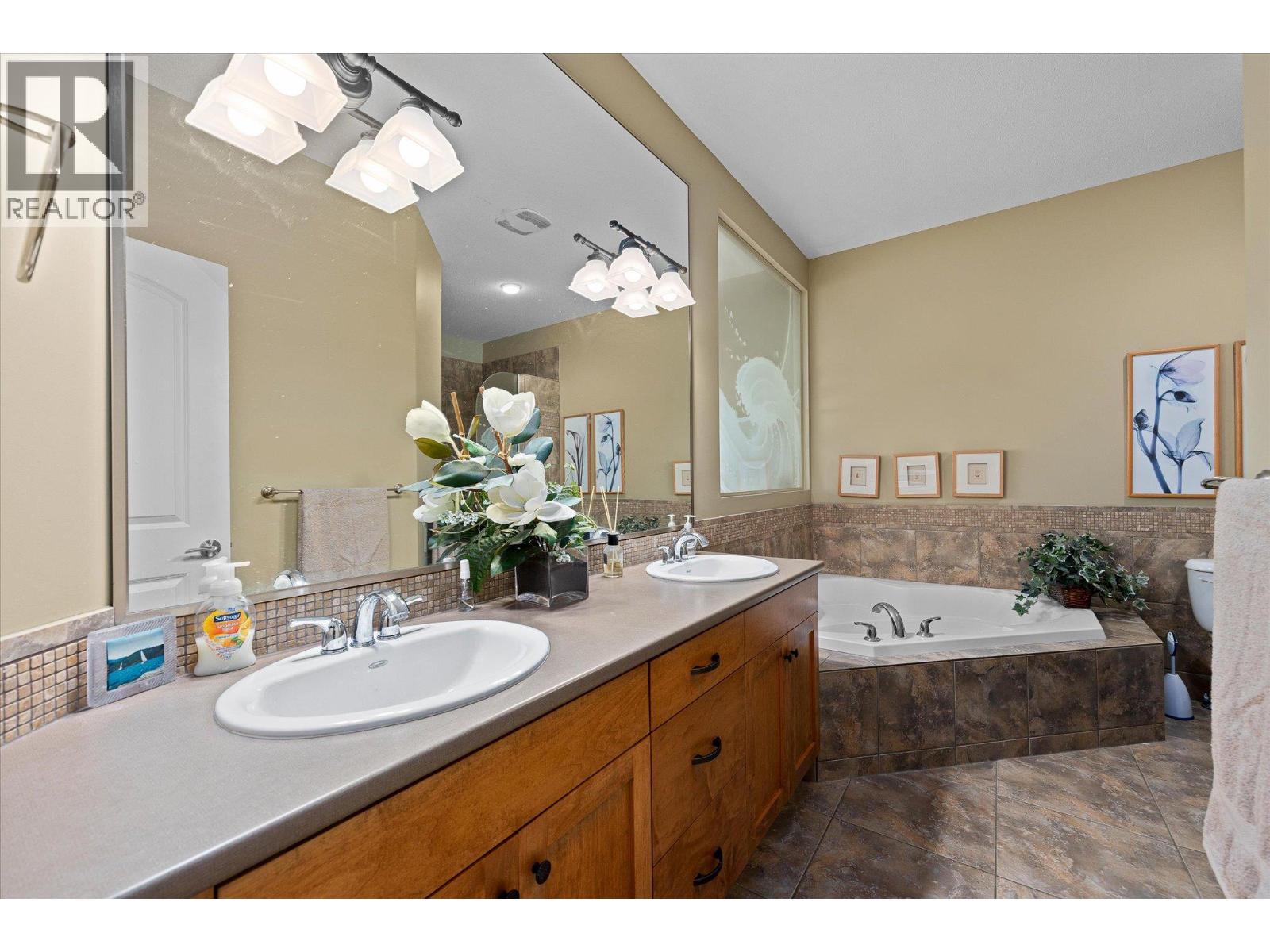 Bathroom with a double-sink wood vanity, large mirror, and tiled corner bathtub.