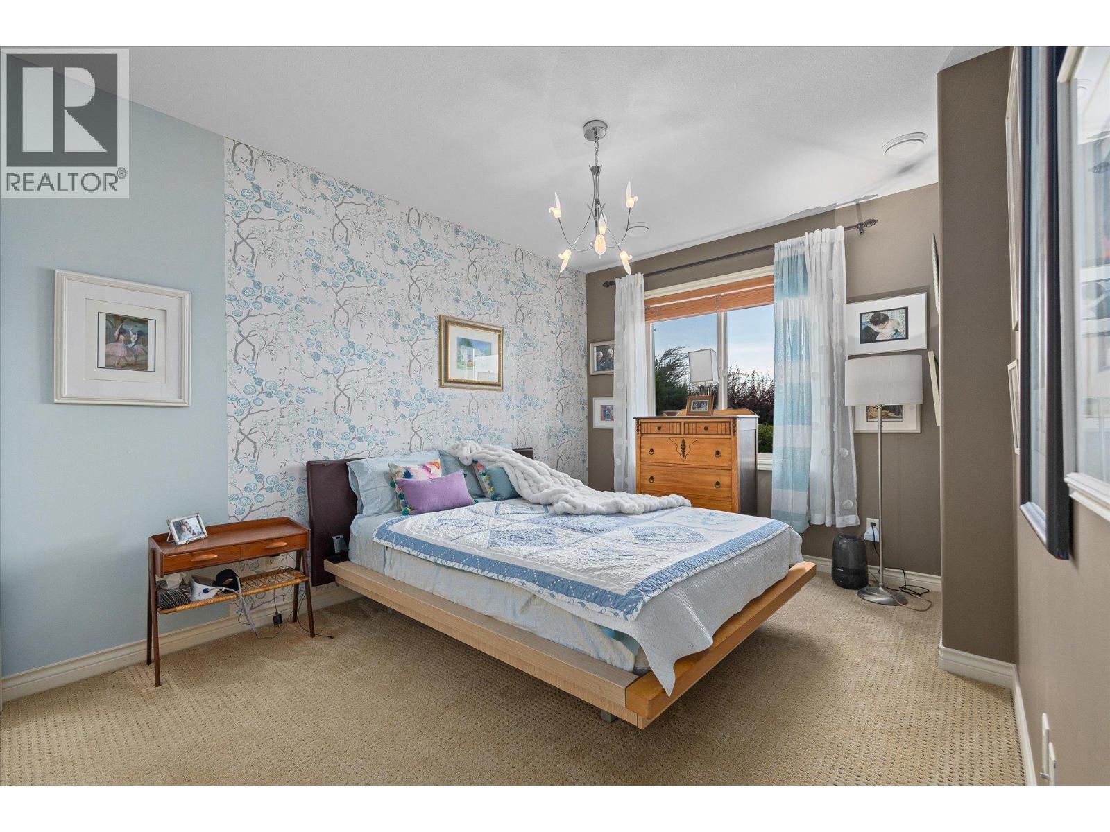 Furnished bedroom with a large bed, patterned accent wall, and bright window.