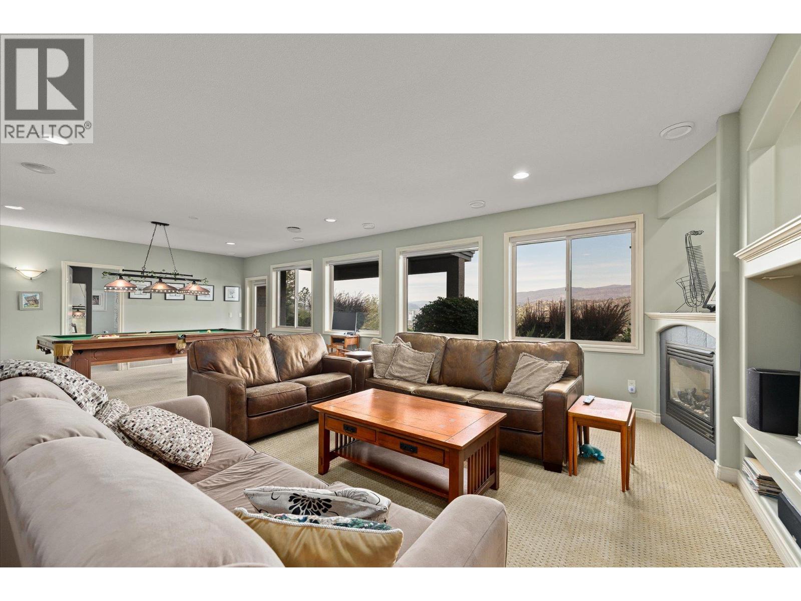 Living room with leather sofas, a pool table, fireplace, and distant mountain views through large windows.