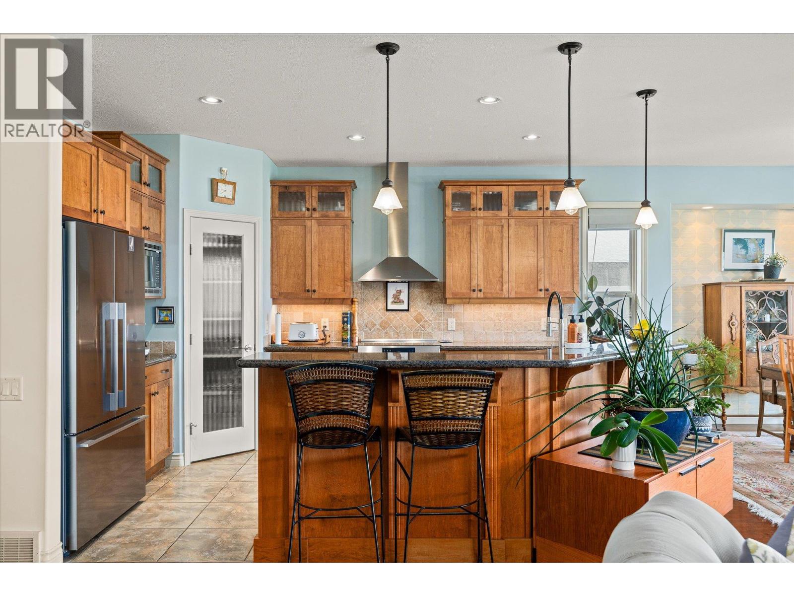 Kitchen with warm wood cabinets, a large island, dark stone countertop, and two bar stools.
