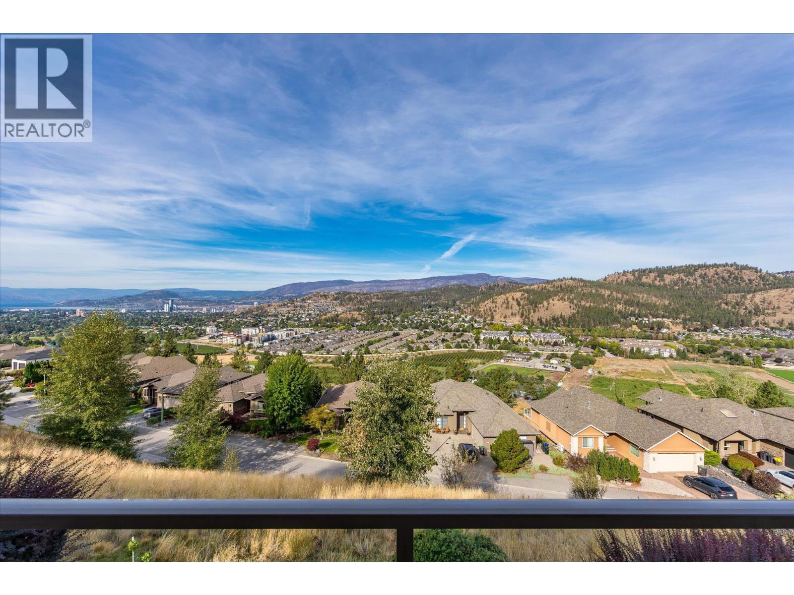 Panoramic view of Kelowna, Okanagan Lake, and surrounding hills from a balcony.