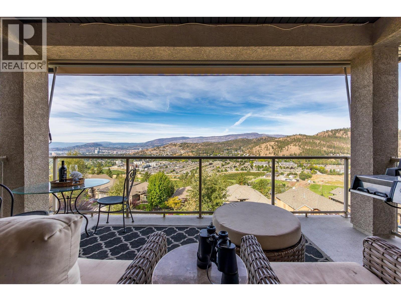Furnished balcony overlooking Kelowna neighborhoods and hills, with a wide view toward the city.