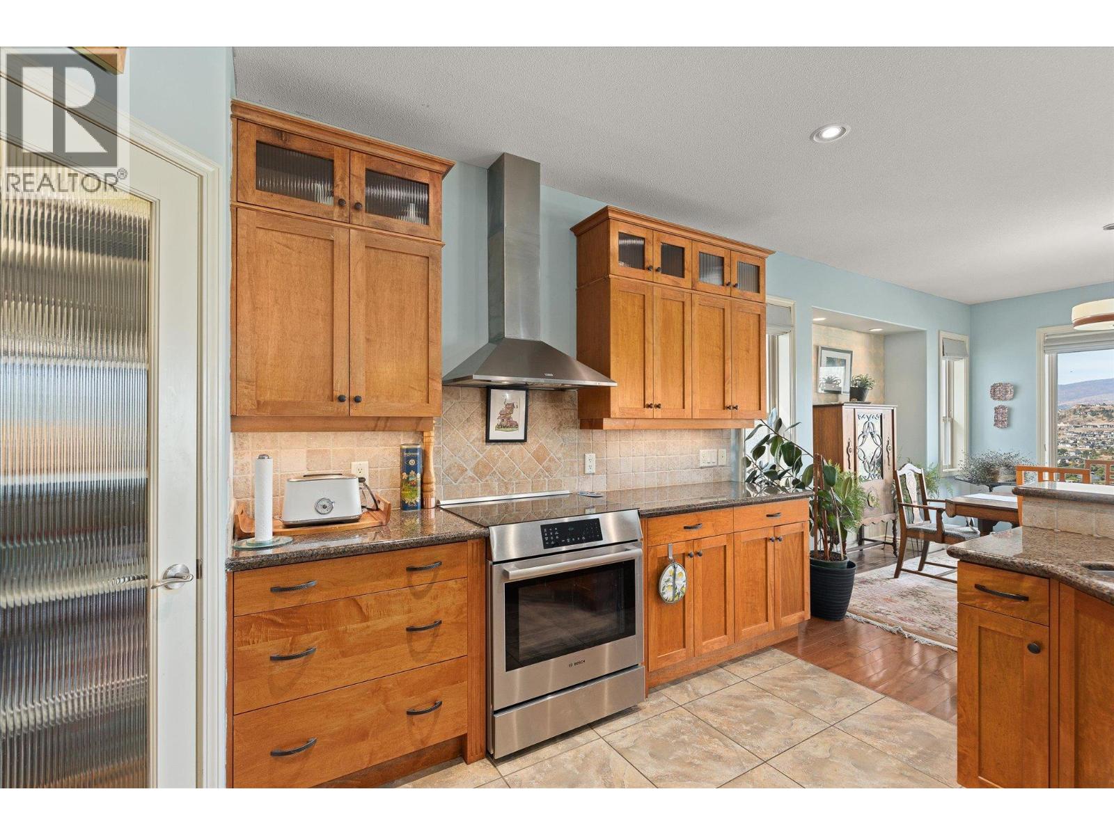 Kitchen with warm wood cabinetry, granite counters, stainless steel range, and adjoining dining area.
