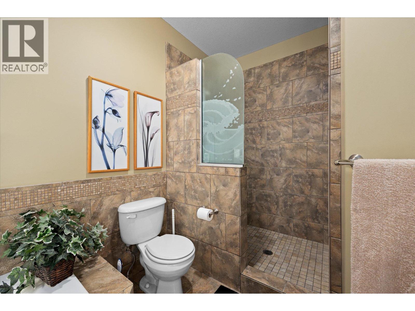 Bathroom with a tiled walk-in shower, curved frosted-glass panel, and brown stone-look walls.