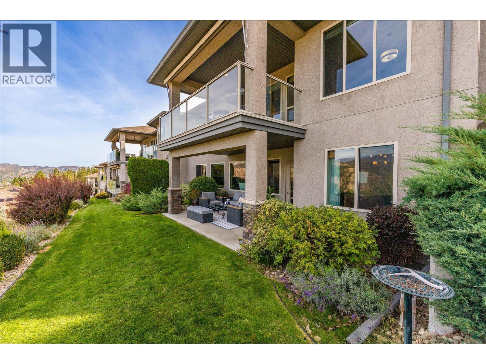 Townhome exterior with glass-railed balconies, landscaped lawn, and covered patio seating.