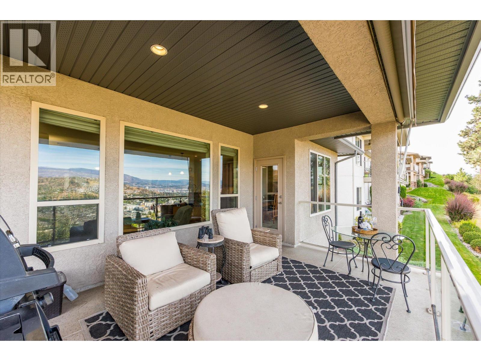 Covered condo patio with wicker seating and a view of Kelowna and distant mountains.
