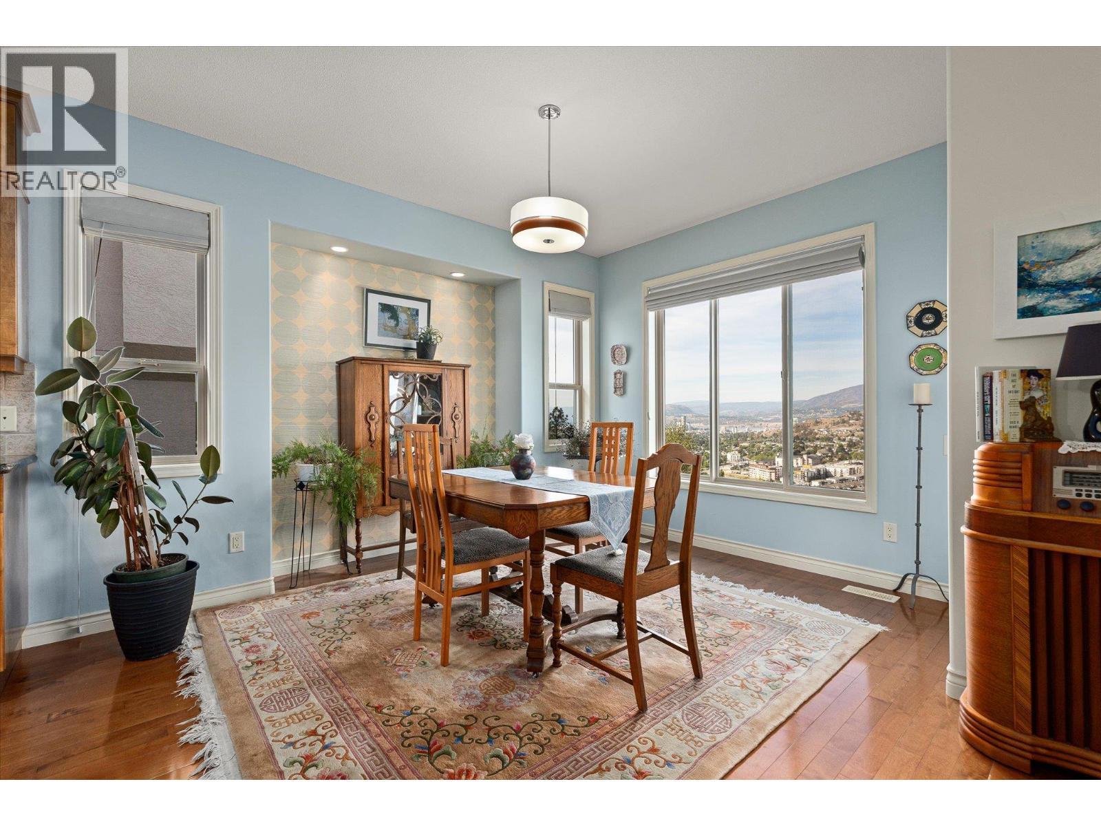 Furnished dining room with wood table, patterned rug, and expansive city-and-hillside views.