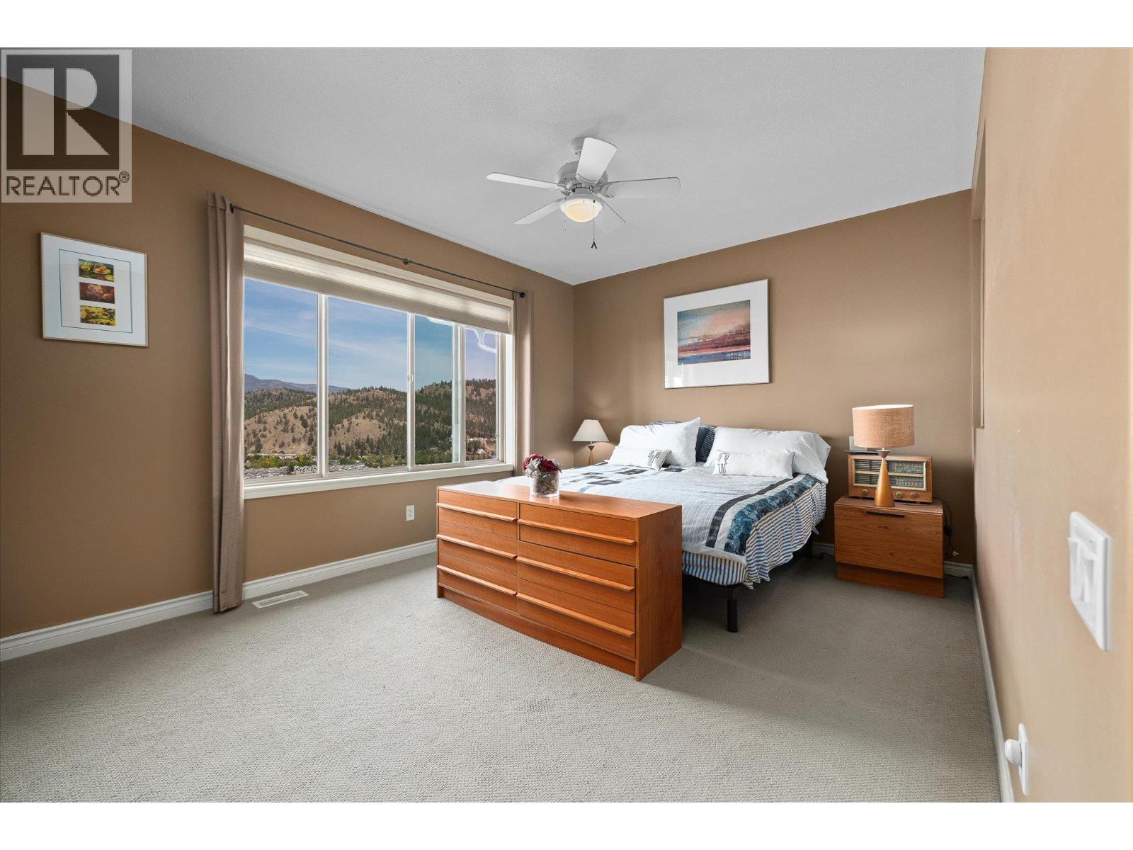 Furnished bedroom with a wooden dresser and a large window overlooking forested hills.